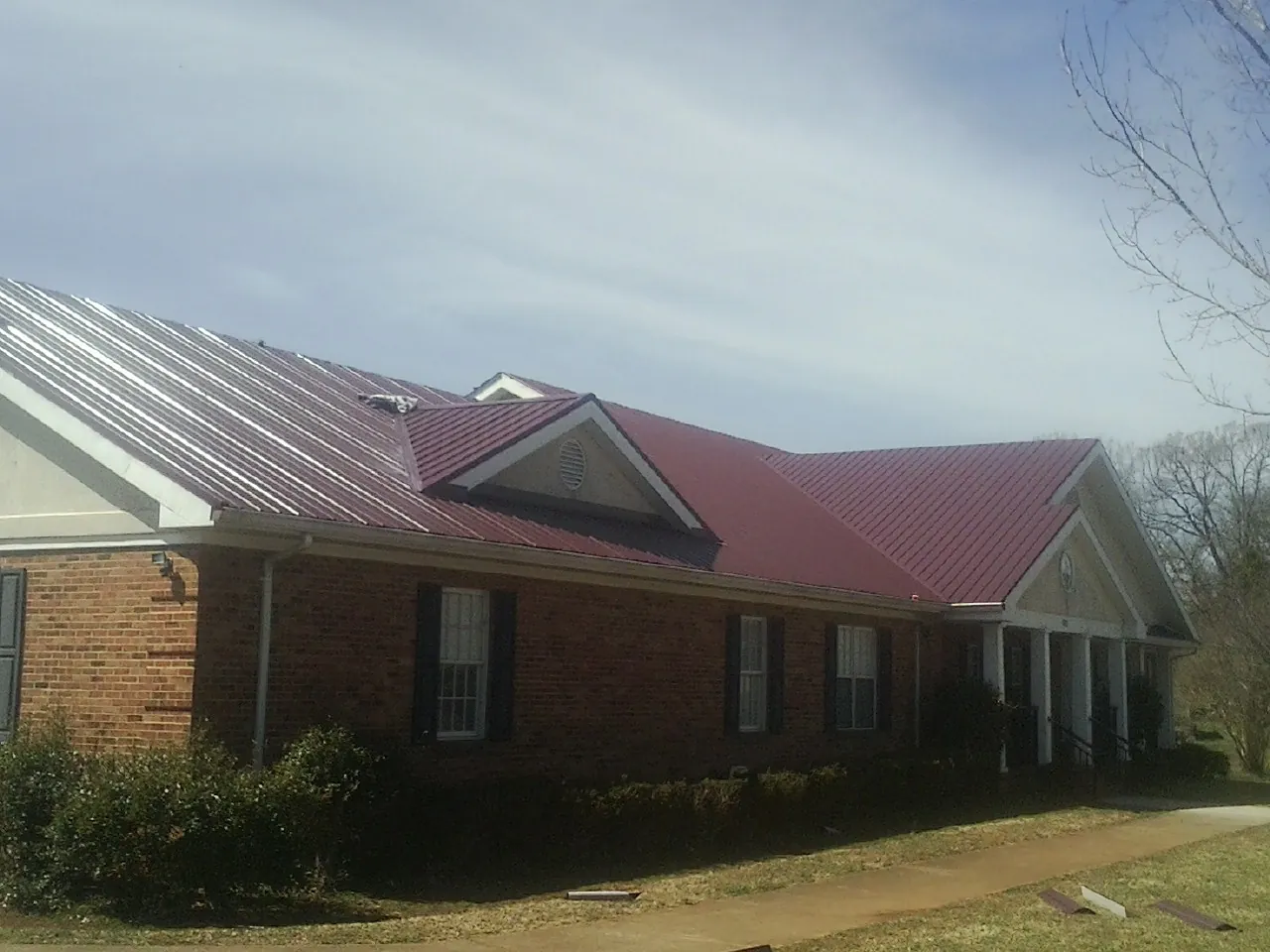 Red metal roof with gabled entries on a long brick building, from a Hail Damage Roof Repair job in Ellwood City