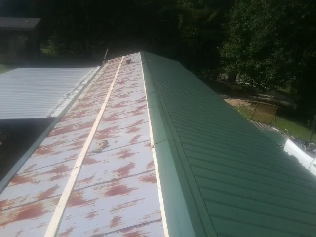 Old rusted panels beside newly installed green metal roofing in Ellwood City
