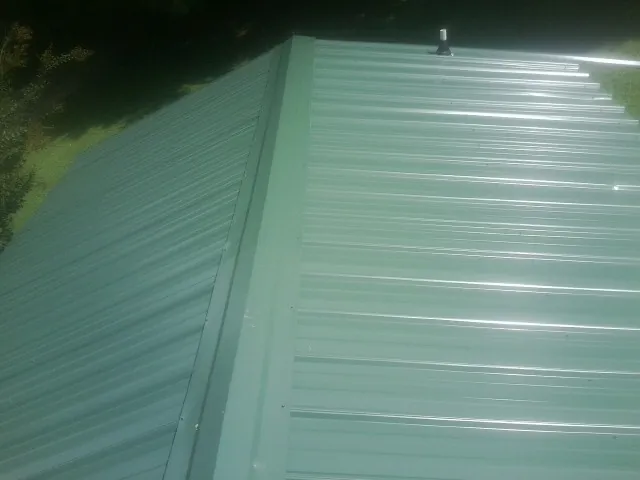 New green metal panels meeting at the ridge of a roof — Flat Roof Repair work by our crew in Ellwood City