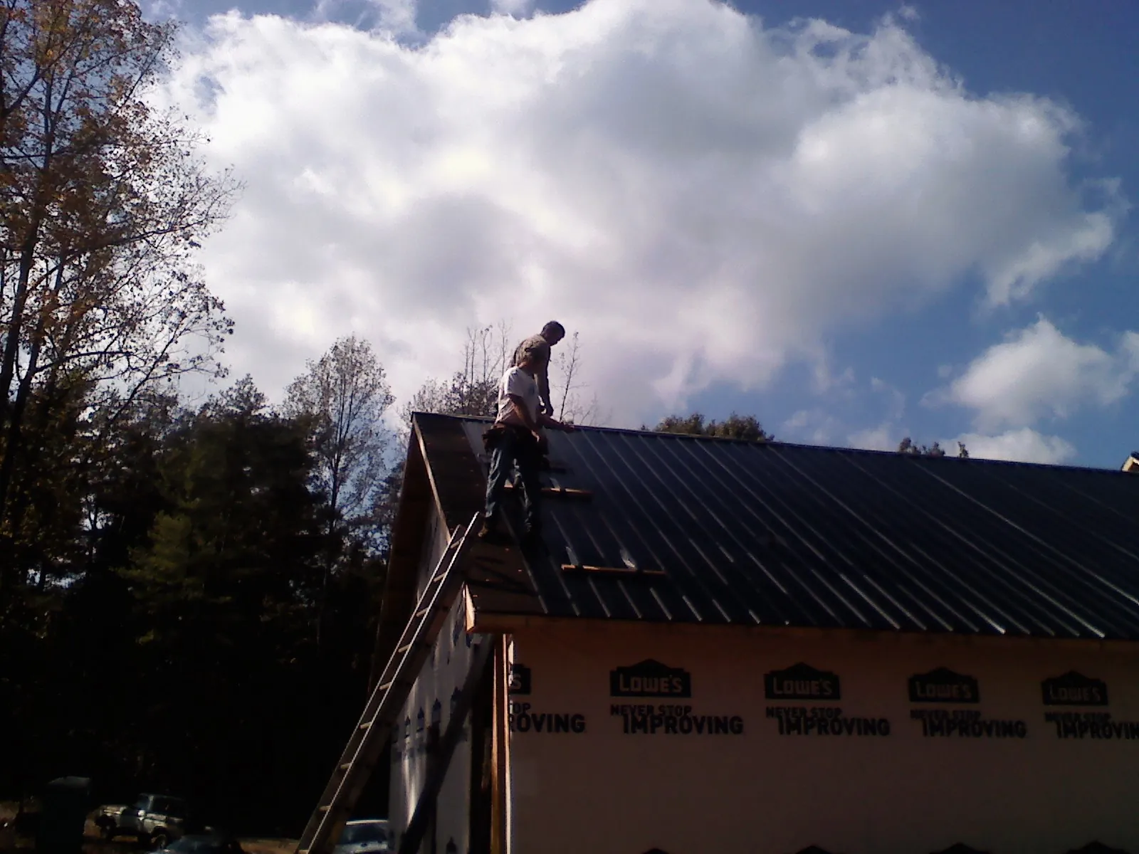Roofer fastening dark metal panels high against a cloudy sky, from a Roof Inspection job in Ellwood City