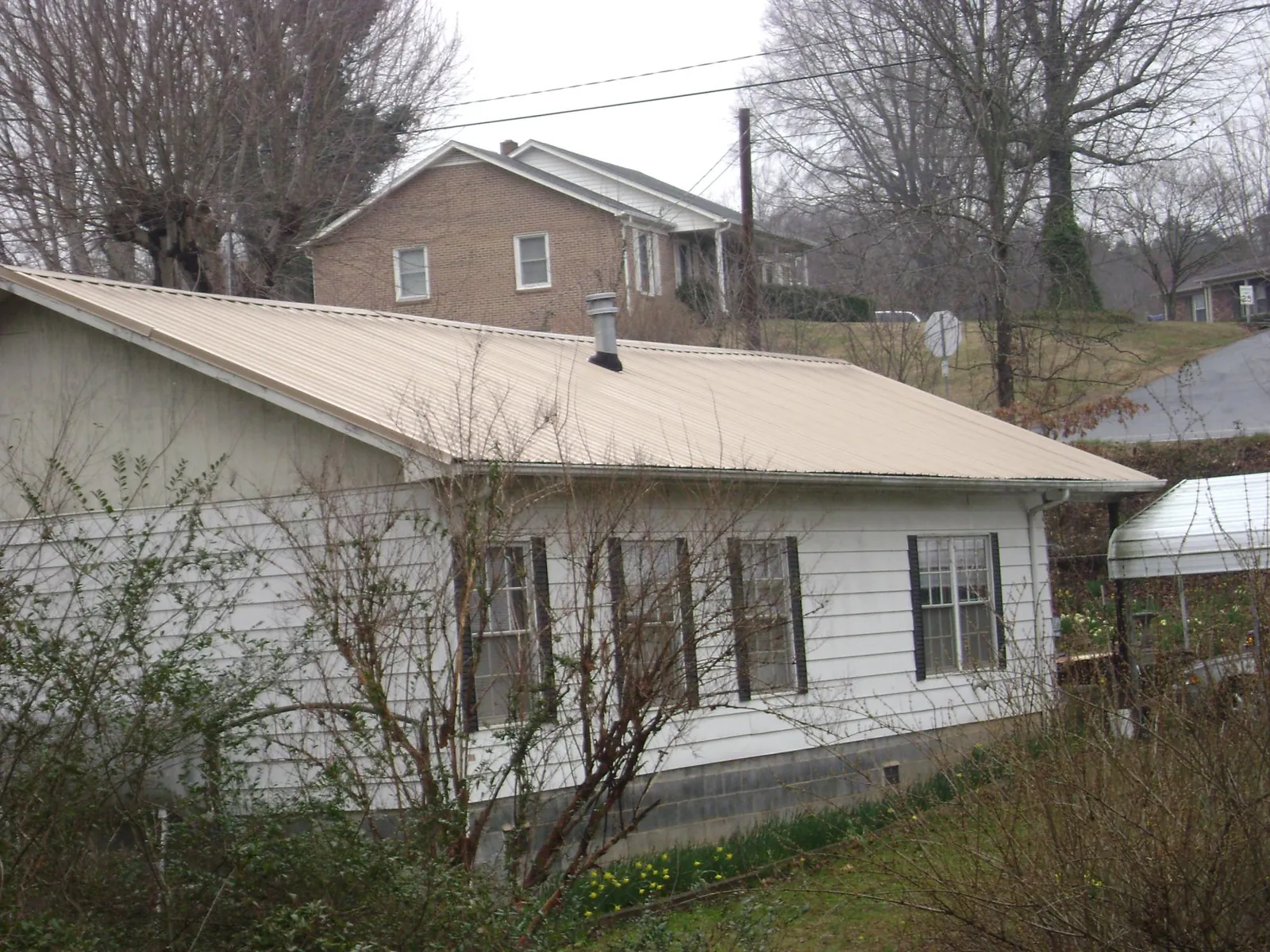 Tan metal roof on a white sided house set into a hillside — Commercial Roofing by Roofing Brothers in Ellwood City