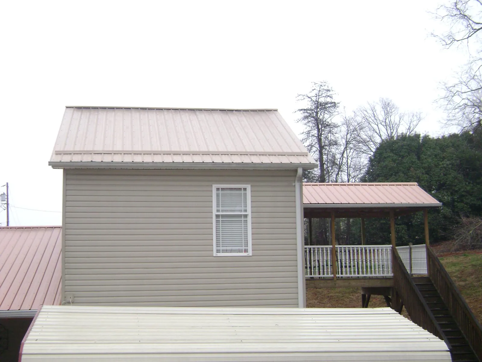 Tan metal roofs on a two story addition and attached porch, from a Roof Replacement job in Ellwood City